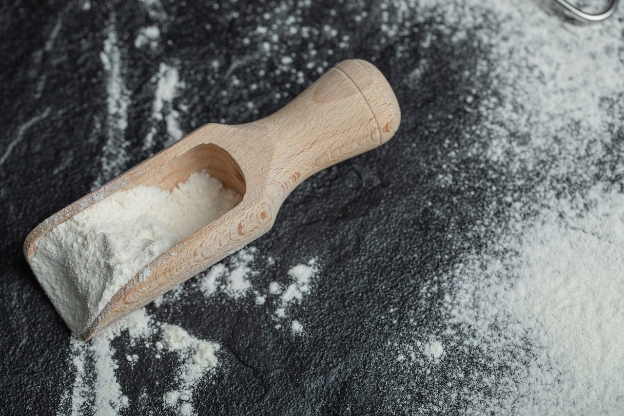 A wooden spoon with flour on a dark background
